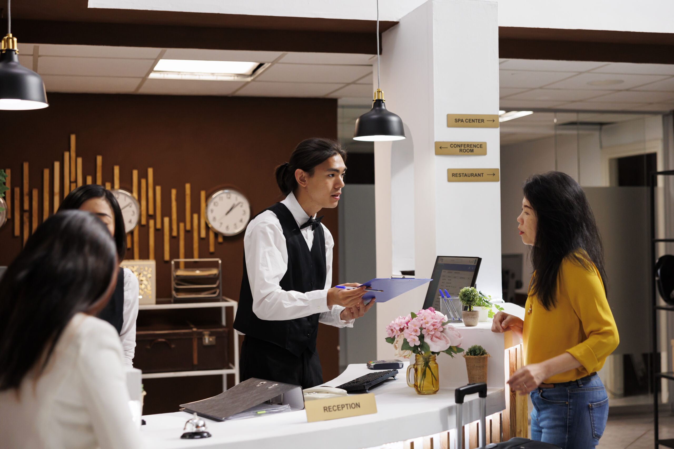 Hotel guest with registration form Hotel guest receiving registration form from helpful asian male concierge. Relaxed asian middle aged woman on vacation making necessary preparation for check in at modern resort
