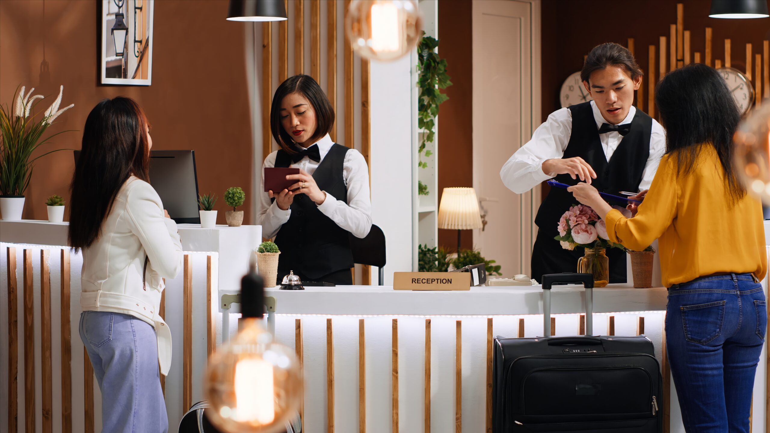 Tourists going through check in process at hotel reception desk, staff verifying passport id for registration. Two women signing ledger and reservation papers for accommodation on trip.
